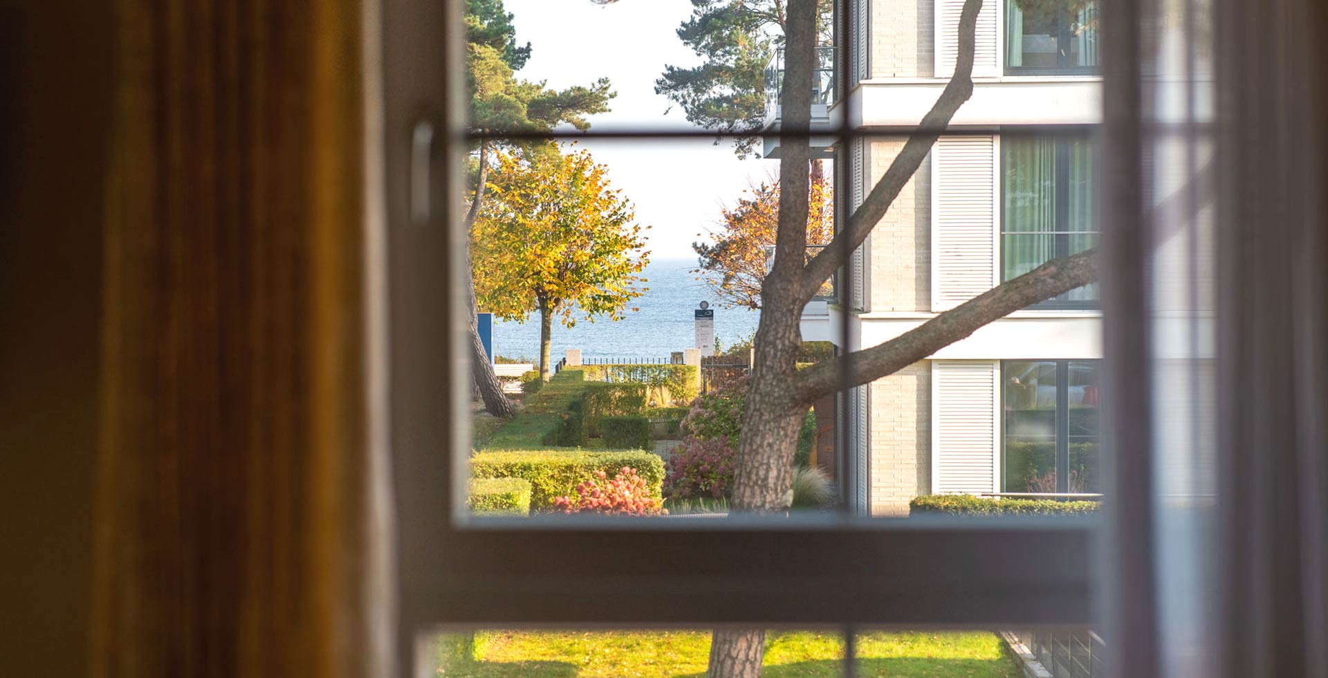 View from the Arkona Strandresidenzen apartment onto the Baltic Sea with garden and autumn trees in Binz